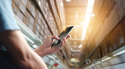 工廠工人使用移動智能手機上的應用來操作現代貿易的自動化。在大型倉庫檢查訂單。海運貨物的進出口。商業營銷與技術